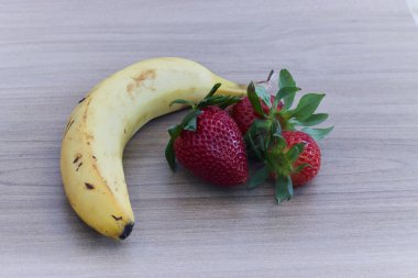 Ahşap bir masada muz ve biraz çilek. Sağlıklı gıda konsepti