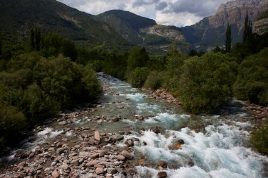Arkasında bulutlu mavi gökyüzü, şeffaf sudan oluşan hızlı akan bir nehir ile dağ manzarası. Ara Nehri, Huesca, İspanya. Yatay çekim