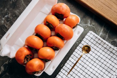 Beyaz bir kabın içinde olgun hurmalar servis edilen mermer bir masada, üst görünümde.