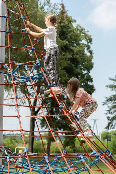 Two elementary school age kids, children climbing a tall structure at the playground together, exercise, healthy physical activity outside, outdoors simple concept, friends, sisters, siblings