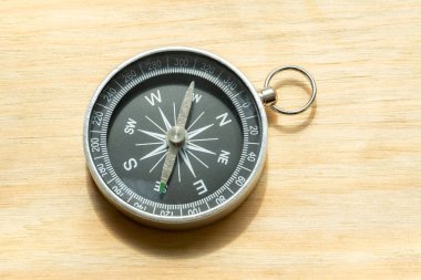 One simple small compass, wayfinding symbol world directions abstract concept, object closeup, natural sun light, laying on a wooden table, detail, up close. Navigation and pathfinding, search, travel