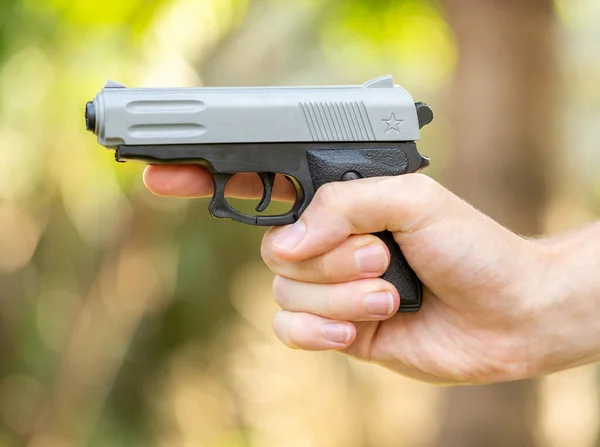 Hand holding a simple small generic plastic toy gun, pistol, fake weapon, side view, finger off the trigger, one person, object closeup, outdoors shot object in hand, closeup. Man holding a toy weapon