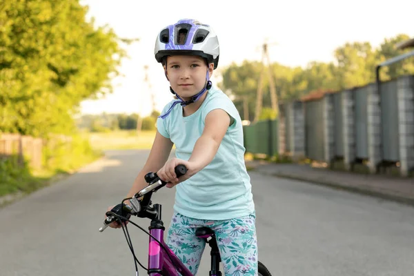 Happy healthy elementary school age girl in a biking helmet, child sitting on a bike smiling, holding the handle bars, looking at camera. Young biker, cyclist portrait, closeup, one person, center