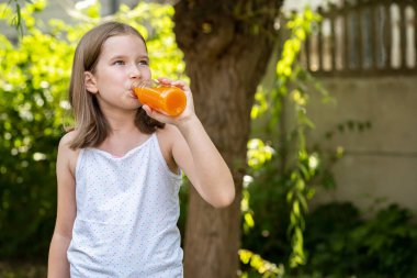 Genç liseli kız, cam şişeden portakal suyu içen çocuk, sağlıklı doğal içecek, vitaminler. Bulanık arkaplan, kopyalama alanı, sağlıklı içecekler reklam konsepti
