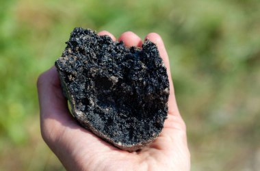 Elinde büyük bir parça siyah asfalt tutan bir adam, yakın plan nesne, detay, makro çekim. Asfalt madde basit konsept, yol yapımı ve otoyol altyapı bakımı. Malzeme mühendisliği