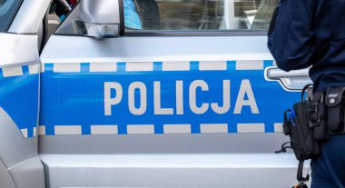 Blue Polish police vehicle and a policeman, policja, police car side detail, closeup. Polish emergency services simple concept, one person, editorial shot clipart