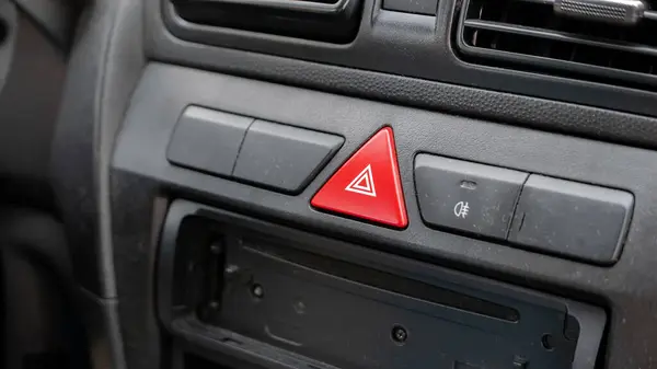 Generic red triangle emergency stop hazard lights button on a car dashboard, car interior object detail closeup, nobody. Vehicle accidents and emergencies abstract concept, old used dusty car inside