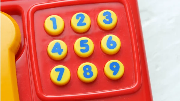 Simple colorful small telephone landline phone toy with little number keys, keypad closeup detail, nobody. Learning numbers, maths, toys for kids and education concept, no people, object up close