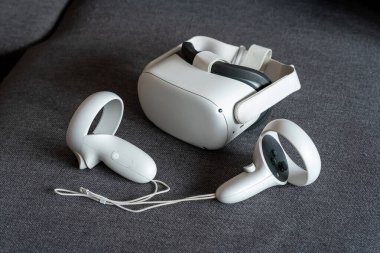 Meta Görev 2 sanal gerçeklik kulaklığı. Kanepede kontrolörler var. Standalone kablosuz ve kablolu VR oyunları ve deneyimleri, teknoloji Metaverse, VR oyun basit kavramı