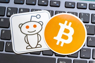 İki çıkartma, biri Reddit logo maskotu, diğeri Bitcoin sembolü, dizüstü bilgisayar klavyesinde, sosyal medyada ve kripto para haber konseptinde, hiç kimse