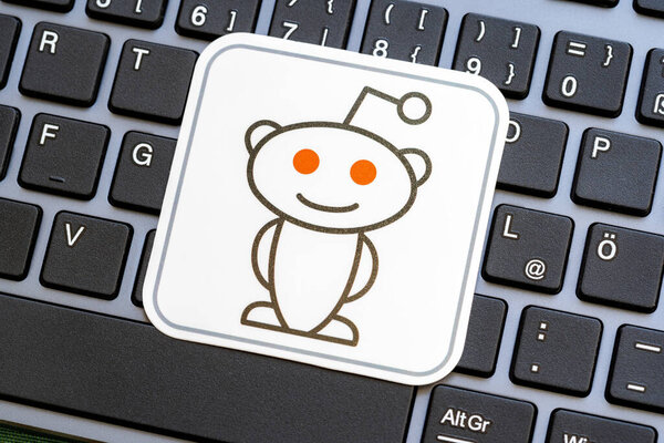 Крупный план логотипа талисмана Reddit Snoo на этикетке наклейки, размещенной на клавиатуре компьютера, в социальных сетях Redditors и subreddits символ культуры, простая концепция, никто