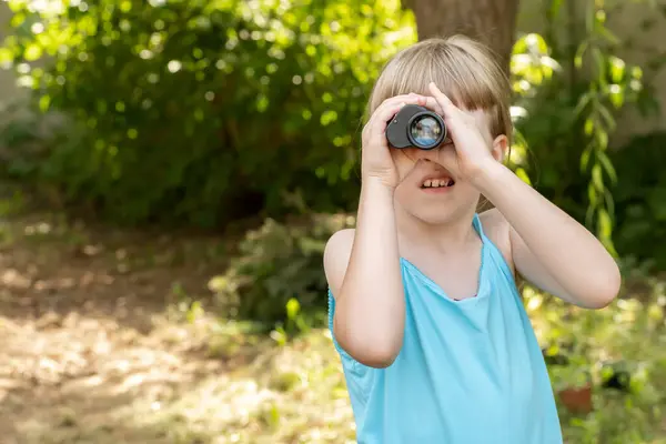 Young child kid uses binoculars to explore the garden, looking for something through the monocular, copy space searching, seeking, spying to find something. Curiosity and exploration simple concept