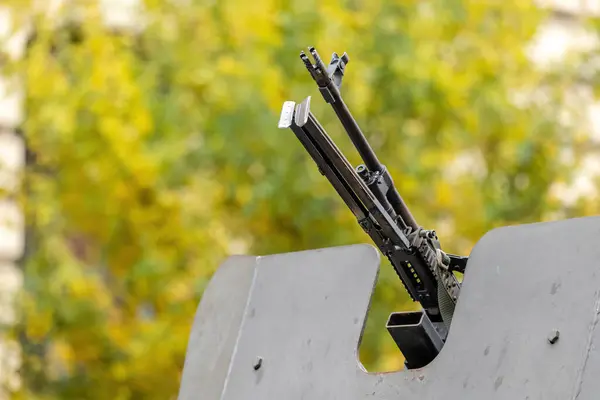 stock image Heavy military machine gun mounted atop an armored vehicle, pointing up, blurred backdrop of green and yellow foliage, army equipment, defense forces, patrol war abstract concept symbol, nobody, news