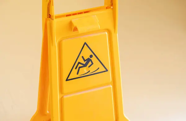 Bright orange wet floor sign is alerting warning of the potential hazard, person falling down icon symbol closeup. Workplace safety education humor simple abstract concept. Injuries at work, in school