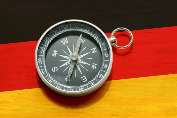 stock image Flag of Germany under a navigation compass laying on a table. German tourism, tour guide business, travel destinations abstract concept symbol, nobody. Exploration, finding a way, career path journey