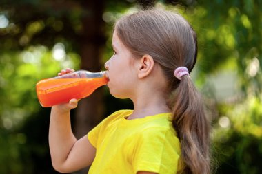 Okul çağındaki kız çocuk çevre dostu cam şişeden meyve suyu içiyor, portre manzarası yakın çekim, güneşli hava, bahar yaz havası. Çocukların beslenmesi, vitaminler, sağlıklı yaşam tarzı.