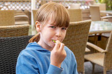 Young girl eating a lime slice in an outdoor cafe closeup portrait of a happy child experiencing sour taste, healthy food choices fresh citrus snack kids nutrition fruit vitamins intake simple concept clipart