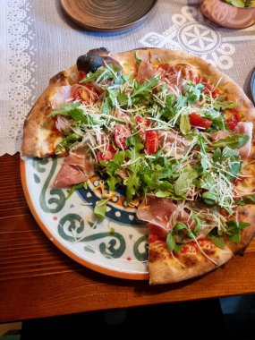 Süslü tabakta roka, prosciutto, vişneli domates ve parmesan peynirli İtalyan pizzası, kısmen yenmiş, birinci şahıs manzaralı, kırsal yemek takımı, yakın çekim, hiç kimse