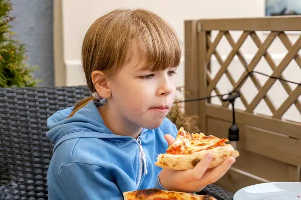 Restoranda pizza yiyen çocuk, pizza dilimi tutan kız, sıradan bir yemek sahnesi, açık hava restoranında oturma, rahatlamış aile yemeği anı, doğal ışıkta yemekten zevk alan çocuk, yakın plan.