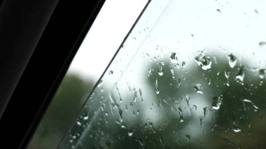 Islak açık araba camına yağan yağmur damlaları, araç camına konan yağmur damlalarına yakın çekim, yağmurda içilen araba yağmuru, penceredeki yağmur suyunun detaylı görüntüsü, fırtınalı hava sürüşü, yağmurlu gün araçlarının iç kısımları.