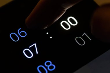 Parmak, dijital akıllı telefon alarmını gecenin 7 'sinde karanlık bir odada modern cep telefonuna ayarlıyor. Sabah erken kalkmak, sabah erken kalkmak zaman kavramı, verimlilik planı, uyku zamanı rutini.