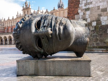 Igor Mitoraj Eros Bendato Krakow Polonya 'da büyük kafa heykeli Büyük Pazar Meydanı Rynek Glowny, Sukiennice tarihi mimari binalar arka planda, açık hava bronz sanat kurulumu, Avrupa