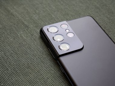 SGS 21 Samsung Galaxy S21 Ultra akıllı telefon bölümünün yakın plan görüntüsü çoklu kamera lensleri makro kamera modülü ve mat siyah kaplama yeşil kumaş yüzey üzerinde, uzay kopyala
