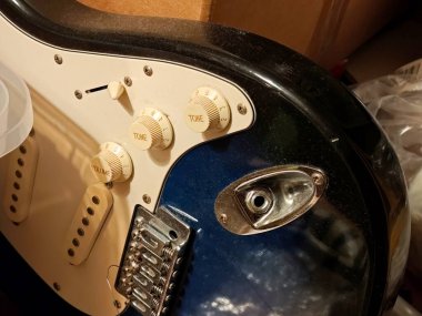 Telleri olmayan eski bir elektro-rock gitar gövdesine yakın çekim. Hasarlı klasik stratocaster strat stil enstrüman detaylarıyla ton ve ses düğmeleri tozlu kullanılmamış müzik teçhizatı depolama konsepti.