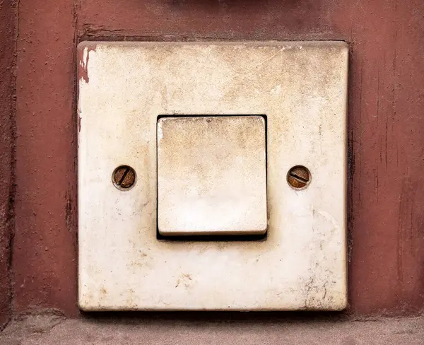 Paslı kırmızı duvar yüzeyindeki eski kirli elektrik düğmesi ya da kapı zili tuşu, eski hasarlı elektrik düğmesi, yıpranmış plastik, bina içi eskimiş, ön manzara, ön çekim detayı