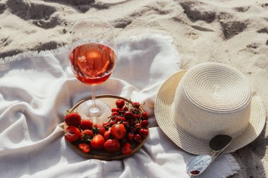 Güneş koruması için ağzına kadar dolgulu saman plaj şapkası bir tabak meyve ve şarapla.