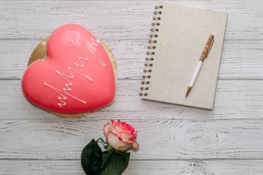 Masada gül ve not defteriyle kalp şeklinde pembe kremalı pasta..