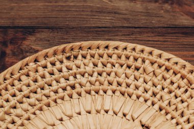 A wicker bowl for decor and fruits stands on a wooden brown table.