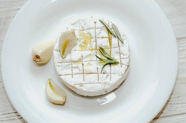 Camembert küflü yuvarlak peynir, biberiye filizi, masada sarımsak..