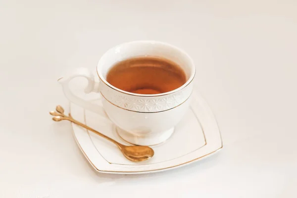 White cup with saucer and golden spoon and tea leaves.