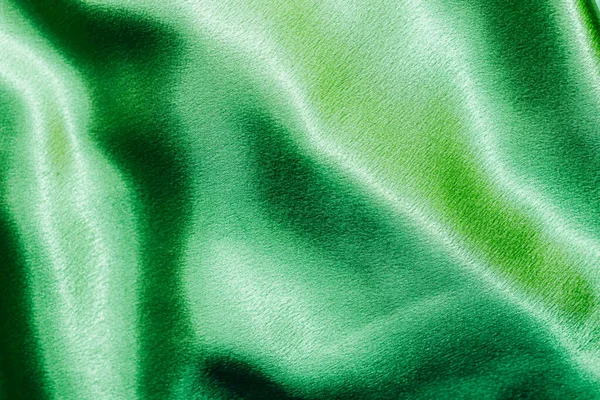 Green shiny texture of silk satin satin with folds.