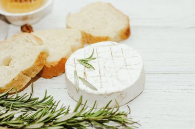 Masanın üzerinde biberiye, bal ve fındık filizi olan camembert küflü yuvarlak peynir.