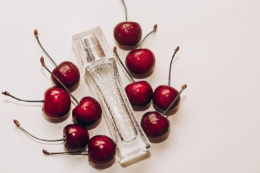 Beyaz masanın üzerinde parfüm şişesiyle olgun kırmızı kirazlar..