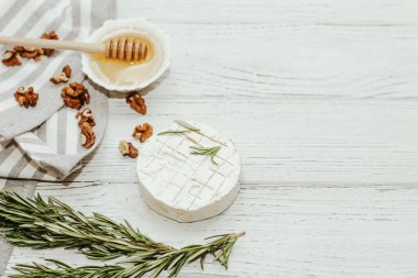 Masanın üzerinde biberiye, bal ve fındık filizi olan camembert küflü yuvarlak peynir.