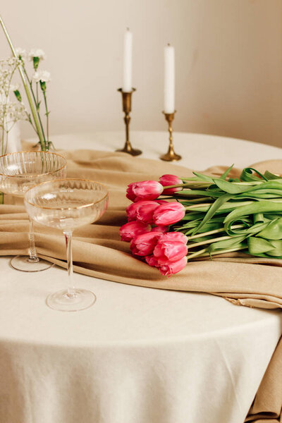 Stylish romantic table setting in the interior with glasses and a bouquet of tulips