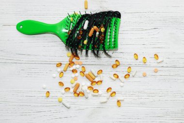 Masaj lambası yeşil fırça, düşmüş saçlar, ahşap arka planda vitaminler..