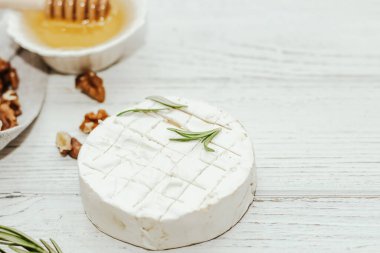 Masanın üzerinde biberiye, bal ve fındık filizi olan camembert küflü yuvarlak peynir.