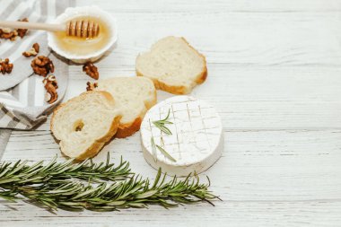 Masanın üzerinde biberiye, bal ve fındık filizi olan camembert küflü yuvarlak peynir.