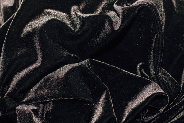 Texture of black velor corduroy fabric with folds.