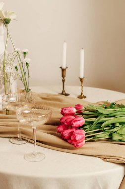 İç mekanda şık bir romantik masa, gözlük ve bir buket lale.