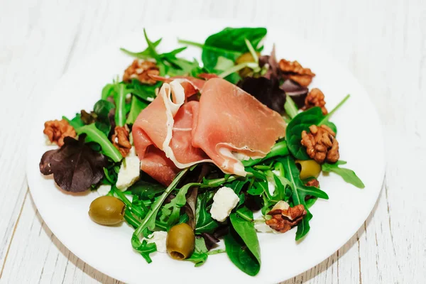 stock image Salad with herbs, arugula, prosciutto, cheese, green olives and nuts.