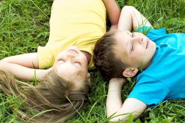 Çocuklar çimenlerin üzerinde yatıyor, elbiseleri sarı ve mavi..