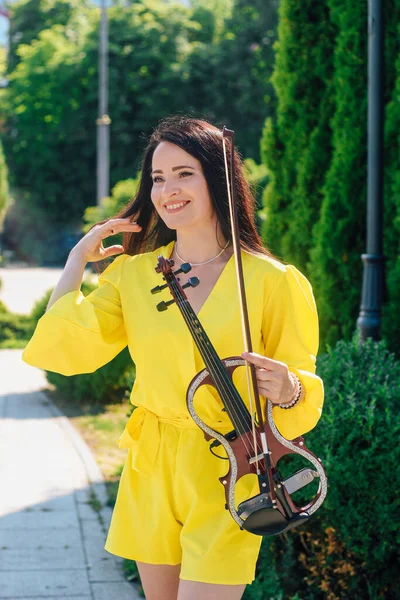 ドレスに暗い髪の女性アーティストが彼女の手に木製のコンサート電気バイオリンを保持しています — ストック写真