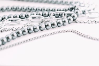 Beyaz estetik arka planda zincir süslemeli gri boncuklardan oluşan bir kolye..