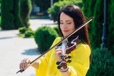 Siyah saçlı, tahta konser kemanı çalan bir kadın sanatçı.