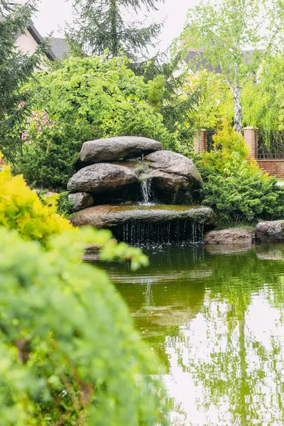 stock image Artificial waterfall of stones and flowers in a landscaped green garden